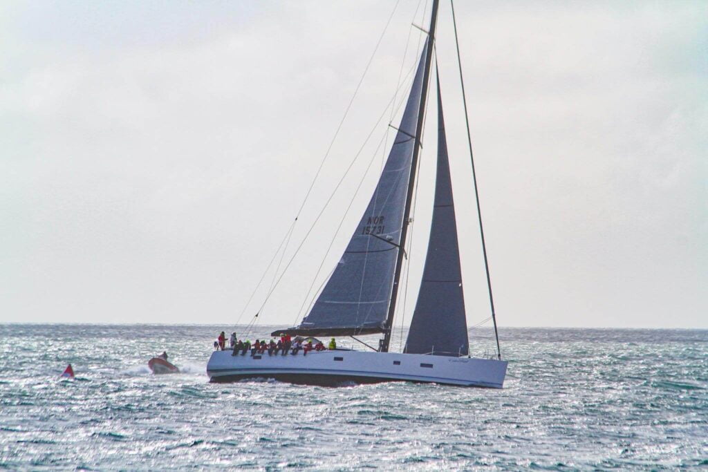 Seilbåt med stort seil som glir over havet, omfavnet av bølger og blå himmel.