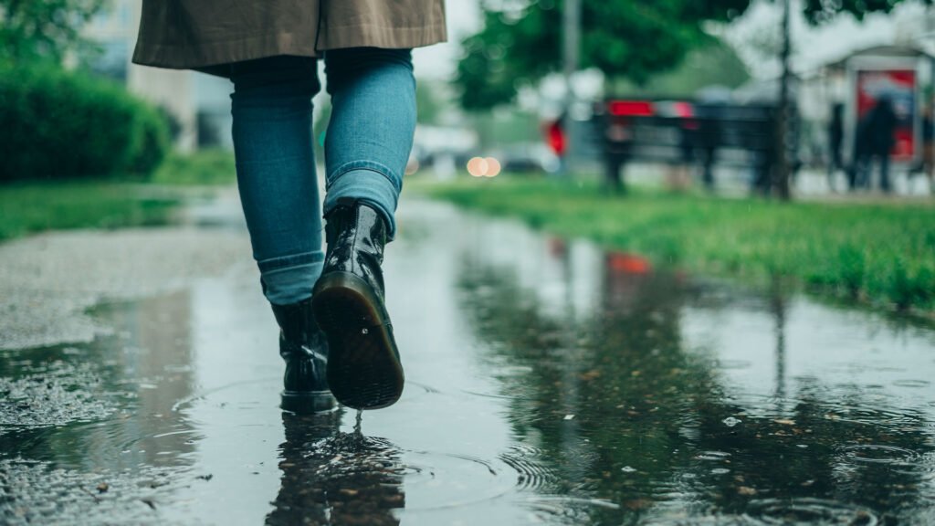 En person går i regnvær med sko, omringet av regnvann som ligger på bakken.