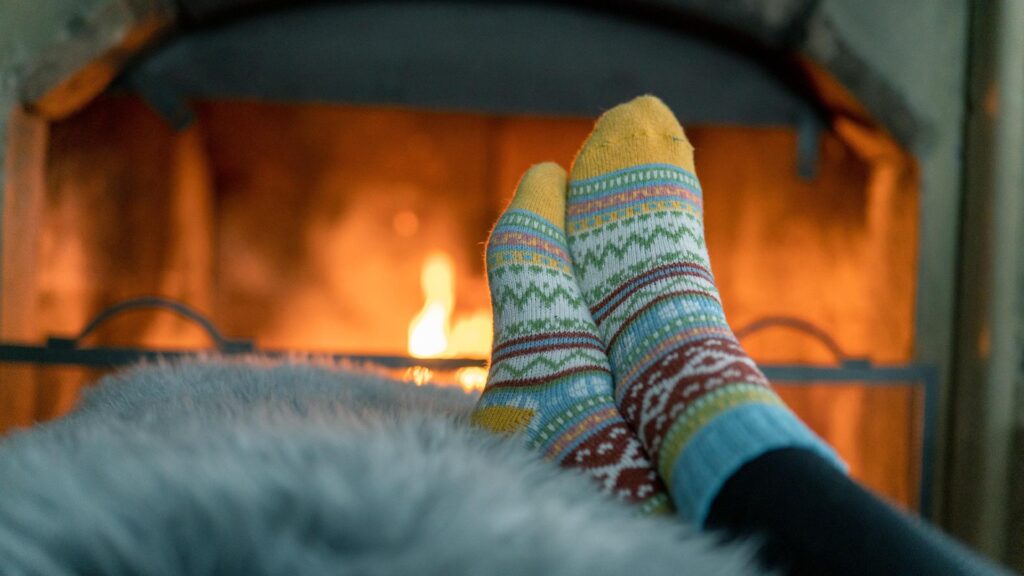 En person sitter med sokker foran en peis, nyter varmen og koselige omgivelser.