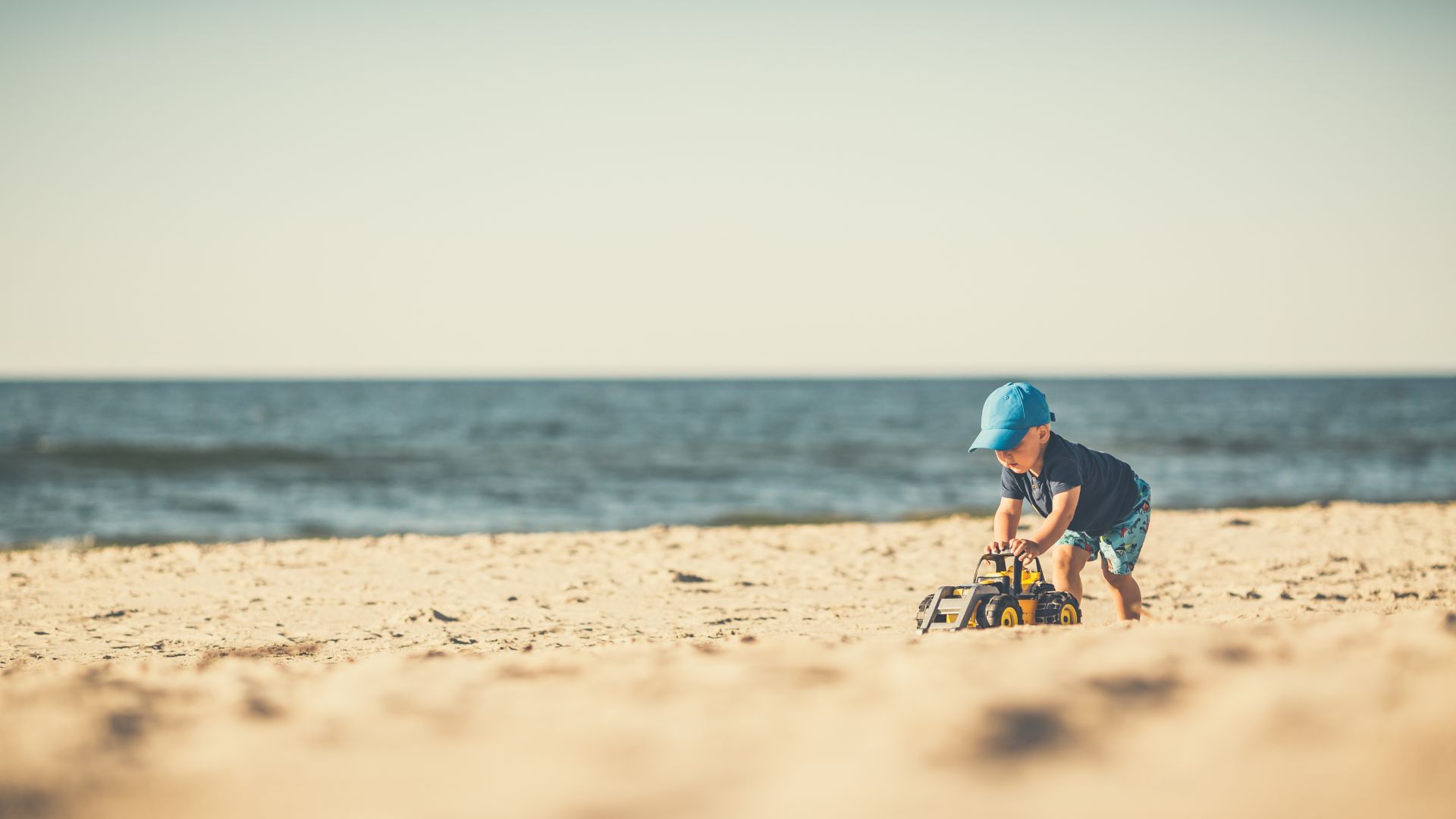 Et lit ebarn leker i sanden på stranden. Foreldrene kan ta det med knusende ro fordi de er Water-Circles-kunder og har tilgang til gratis legehjelp fra Helsetelefonen 24/7.